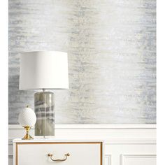 a lamp sitting on top of a white dresser next to a wallpapered wall