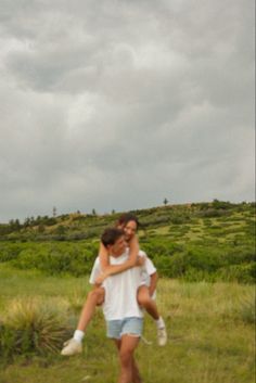 two people hugging each other in the middle of an open field with grass and bushes