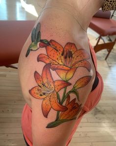 a woman with a tattoo on her back has orange lilies and a green humming