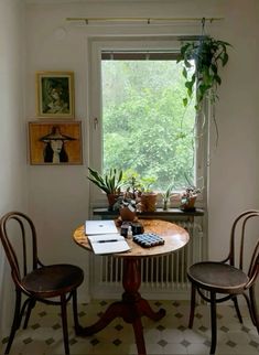 two chairs sitting at a table in front of a window with potted plants on it