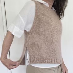 an older woman wearing a sweater vest and glasses standing in front of a white wall