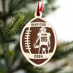 a wooden ornament hanging from a christmas tree with a football and the name hawk eyes on it