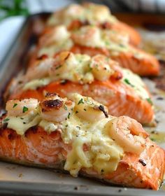 three salmon fillets on a baking sheet covered in sauce and garnished with shrimp