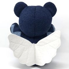 a blue teddy bear with white wings on it's back, sitting in front of a white background