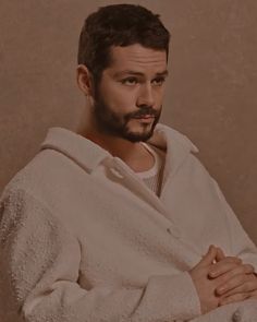 a man with a goatee in a bathrobe looking at the camera while holding his hands on his chest