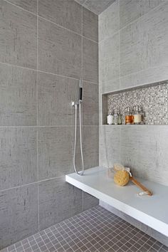 a bathroom with gray tiles and white counter tops, including a shower head in the corner