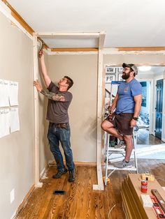 two men working on an unfinished wall in a room with wood floors and hard wood flooring