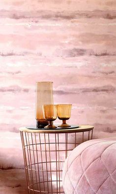 a table with two glasses on it next to a pink ottoman and wallpapered background