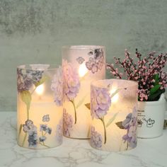 three lit candles sitting on top of a table next to flowers and a potted plant