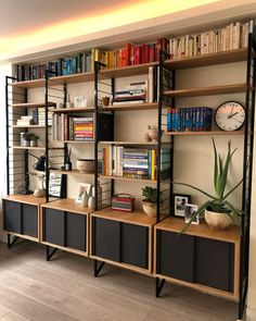 a bookshelf filled with lots of books next to a wall mounted clock and plant