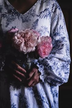 a woman wearing a blue and white dress holding a bouquet of pink carnations