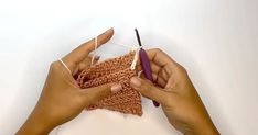 two hands holding yarn and crochet hooks over the top of a piece of cloth