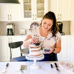 a woman standing in front of a cake on top of a white table with utensils