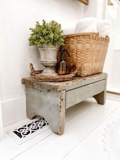 an old wooden bench with baskets and towels on it in front of a white wall