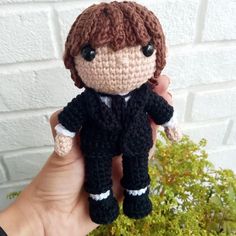 a crocheted doll is being held in front of a brick wall and plant