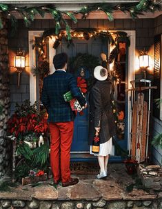 a man and woman standing in front of a blue door with christmas decorations on it