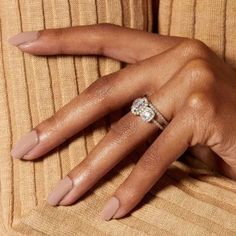 a woman's hand with a diamond ring on her left hand, wearing a tan sweater