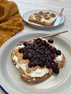 a white plate topped with bread covered in blueberries and whipped cream next to a fork