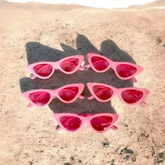 five pink sunglasses laying in the sand at the beach