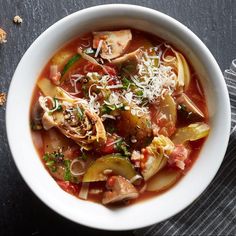 a white bowl filled with vegetable soup on top of a black table next to a spoon