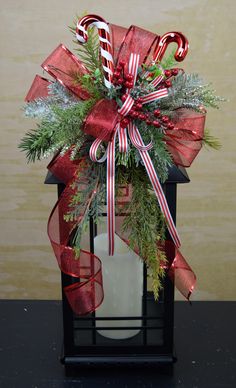 a christmas decoration with candy canes and greenery in a black lantern holder on a table