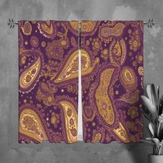 two purple and gold paisley curtains hanging on a wall next to a potted plant