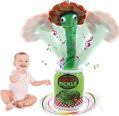 a baby sitting on the ground next to a green pickle toy with music notes coming out of it