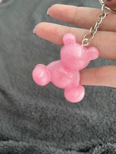 a pink teddy bear shaped keychain hanging from a person's hand