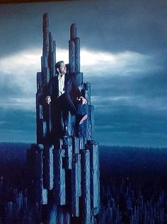 a man in a suit sitting on top of a giant piece of wood with his hands out