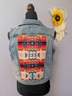 the back of a jean jacket with an orange and blue pattern on it, next to a sunflower