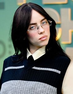 a woman wearing glasses and a sweater looks off to the side while standing in front of a sign