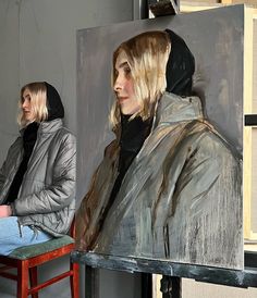 two people standing in front of a painting on a easel and one person sitting at a table