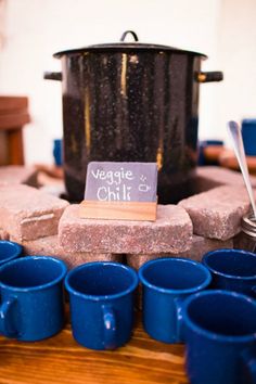 blue cups sitting on top of a wooden table next to a black pot and sign