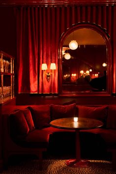 a red couch sitting in front of a window next to a table with a lit candle on it