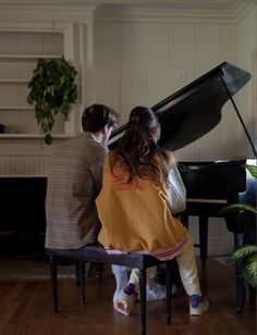 two people sitting on a bench playing piano