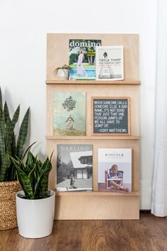 a wooden shelf filled with magazines and books next to a potted plant on top of a hard wood floor