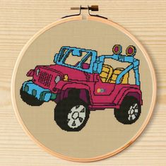 a cross stitch pattern with a pink jeep in the front, on a wooden surface