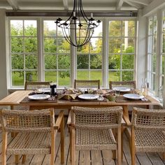 a dining room table with chairs and plates on it, in front of large windows