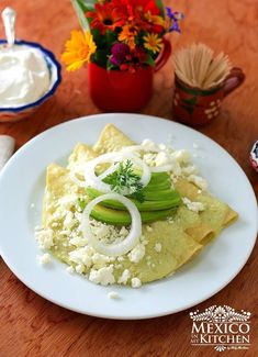 a white plate topped with nachos covered in cheese and onions next to flowers