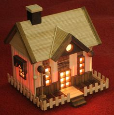 a small wooden house with lights on the front and side windows, sitting on a red carpet