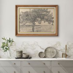 a painting hanging on the wall above a white cabinet with drawers and bowls in front of it