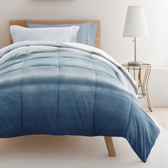 a bed with blue and white comforters in a room next to a lamp on a table