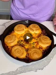 a woman standing in front of a skillet filled with food