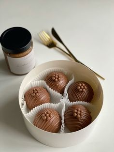 four chocolates in a white bowl next to a jar of peanut butter and a spoon