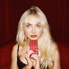 a woman with blond hair holding a red object in front of her face and posing for the camera