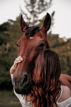 a woman standing next to a horse with her hand on the face of it's head