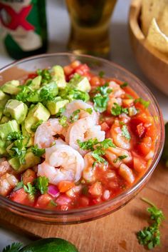 a glass bowl filled with shrimp, guacamole and tortilla chips