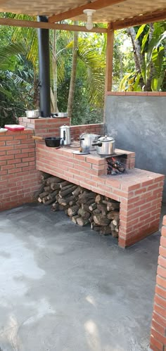 an outdoor kitchen made out of bricks and stacked firewood with pots on the stove