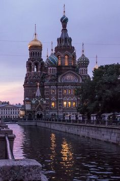 an old church is lit up at night by the water's edge with its reflection in the water