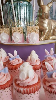 several cupcakes with pink frosting and bunny ears on them sitting in front of a cake